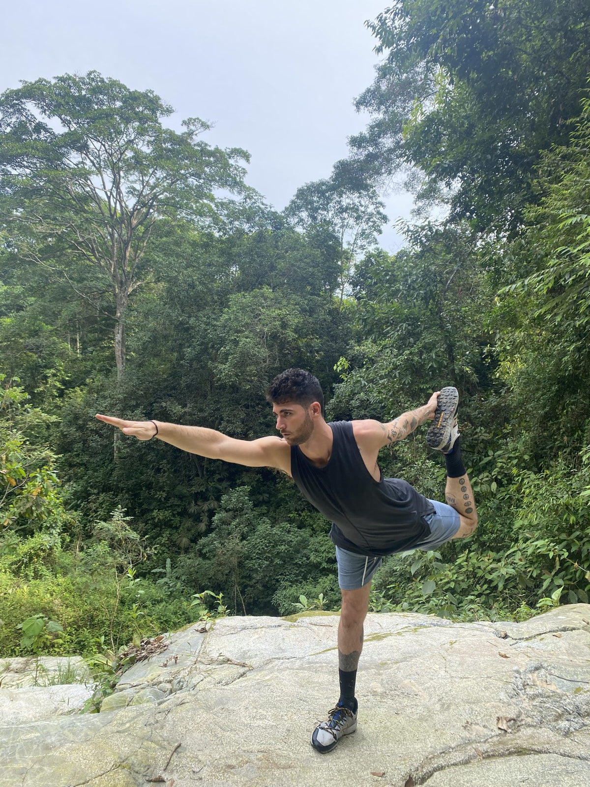 Blake in a standing yoga balance on a rock in the rainforest